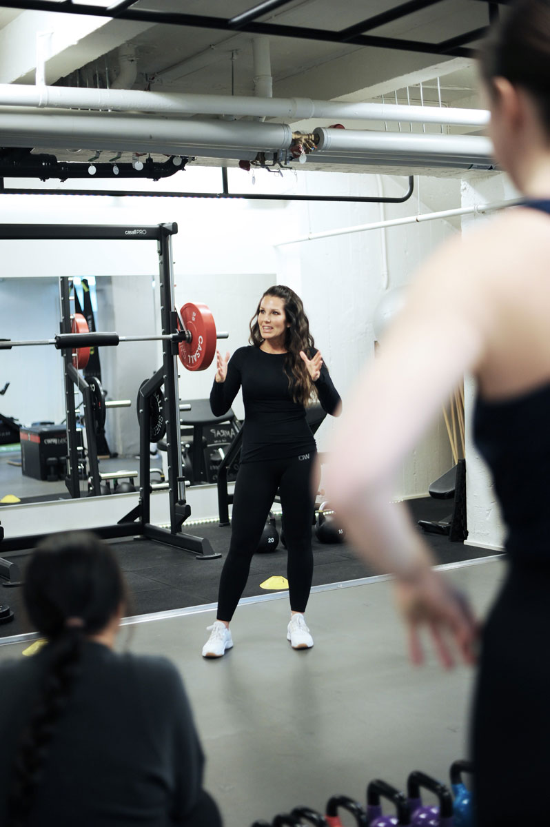 Tränaren sitter på en bänk i ett gym och dricker en hälsosam dryck efter träningen.
